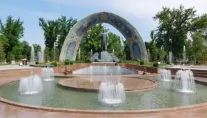 Statue of Abu Abdallah Rudaki standing under a grand colorful mosaic arch surrounded by fountains in Rudaki Park, Dushanbe, Tajikistan.
